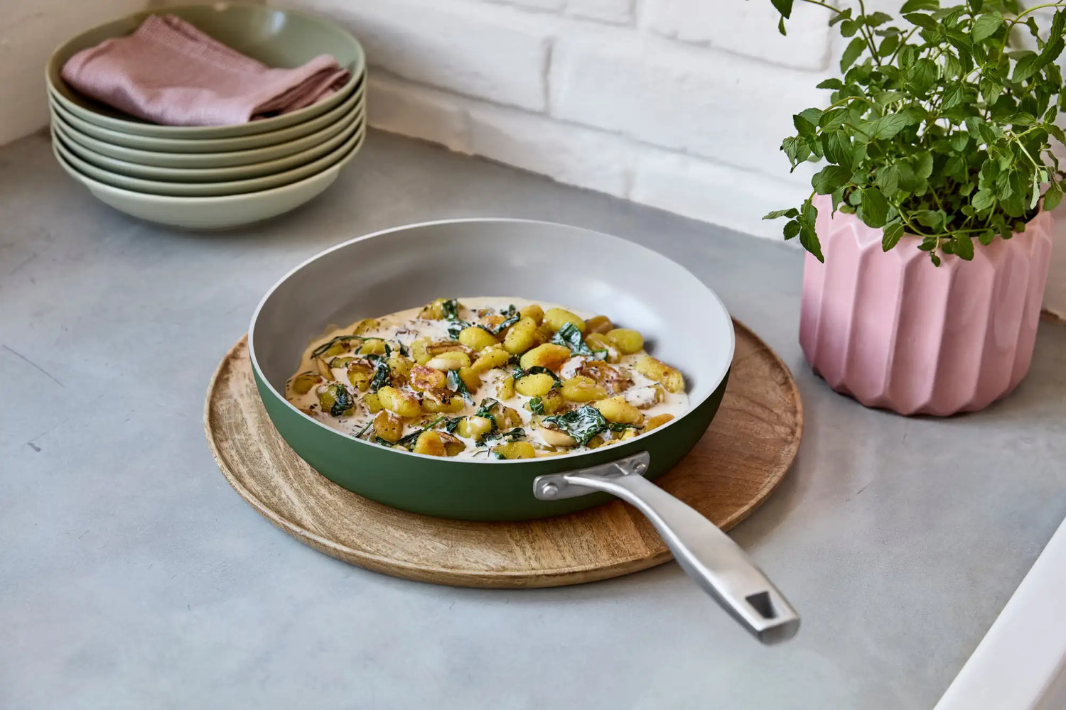 Zeleno-bílá nepřilnavá pánev s dřevěným podstavcem.